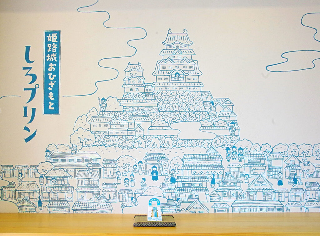 城下町の中にプリン屋やプリンを食べている人などが描かれている楽しいイラスト